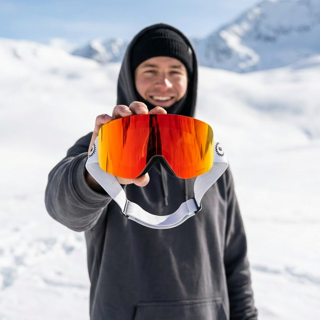 Person holding up a pair of Solaro Shades ski goggles with a snowy mountain background