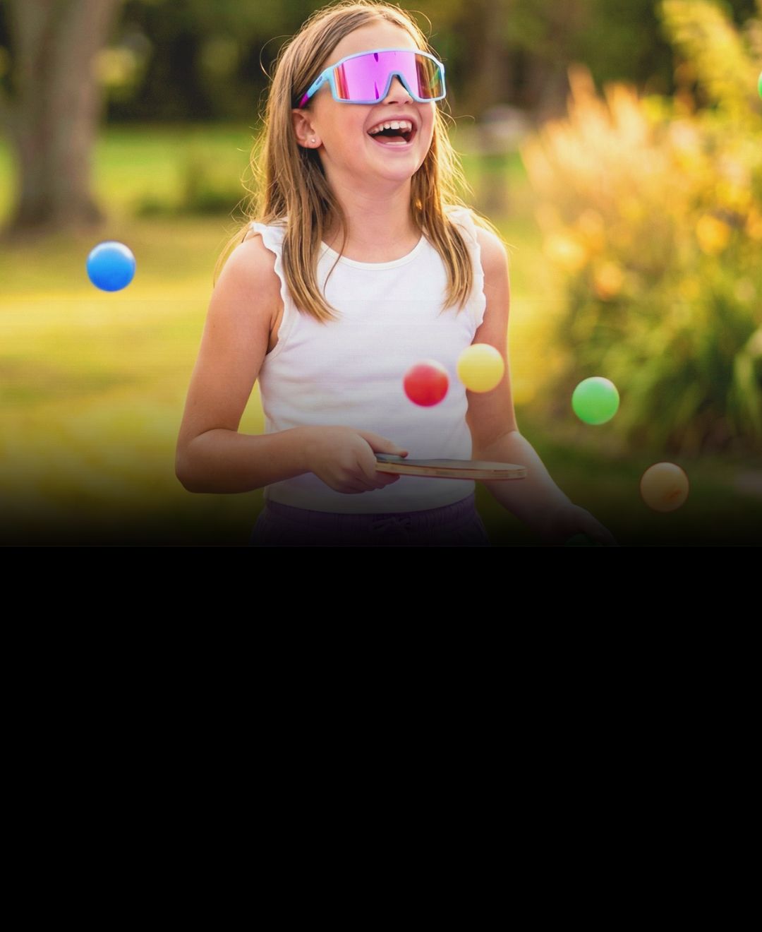 Child juggling colorful balls outdoors on a sunny day wearing Solaro Shades youth sunglasses.