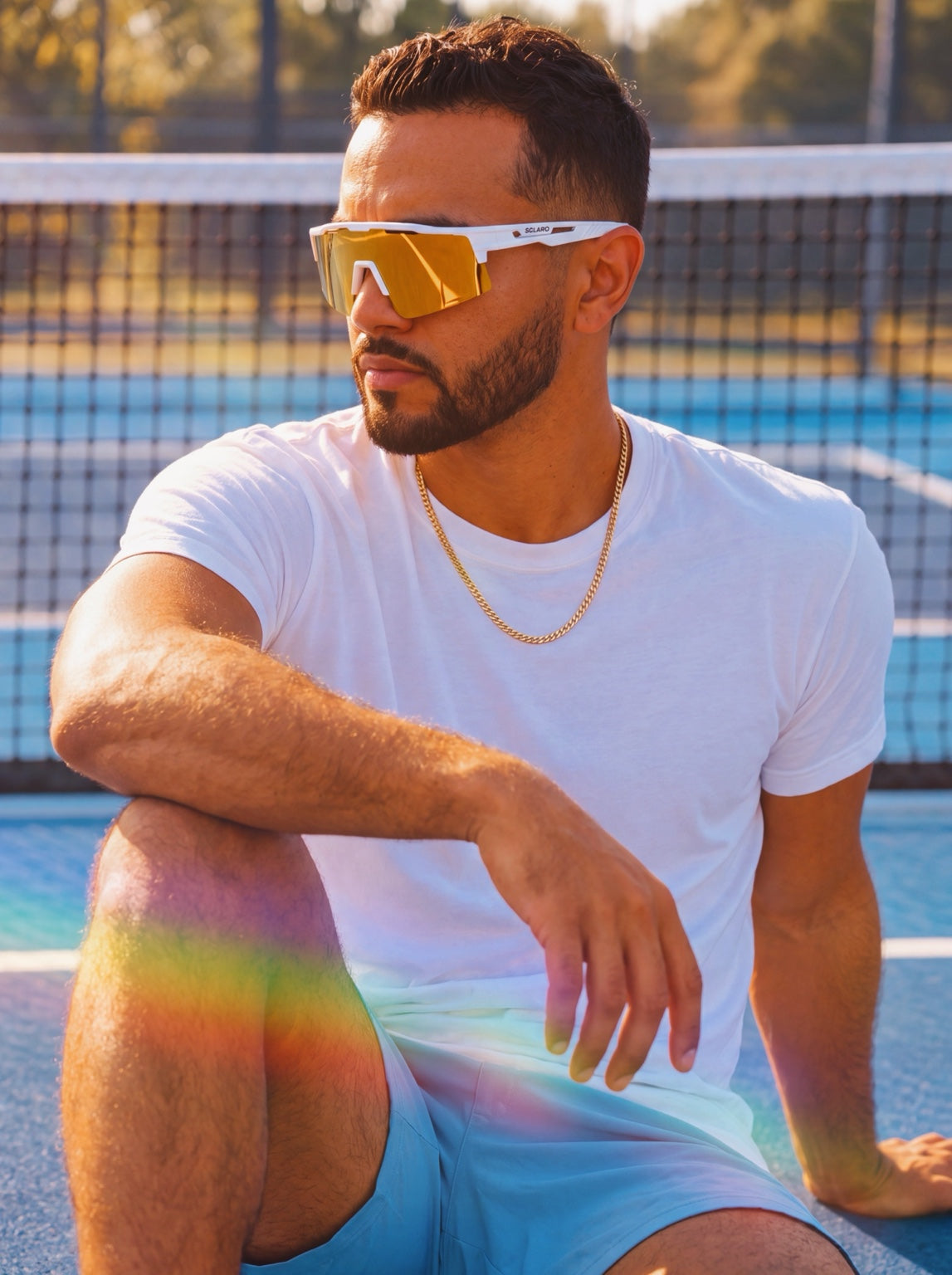 Man wearing white Solaro sunglasses with gold mirrored lenses on a blue court