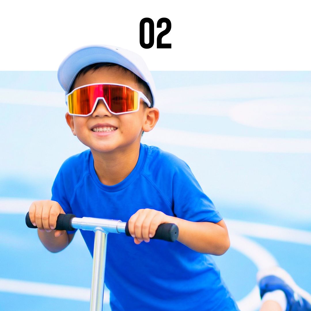 Child wearing Solaro Shades kids sunglasses and a blue shirt and colorful sunglasses riding a scooter with a clear sky background