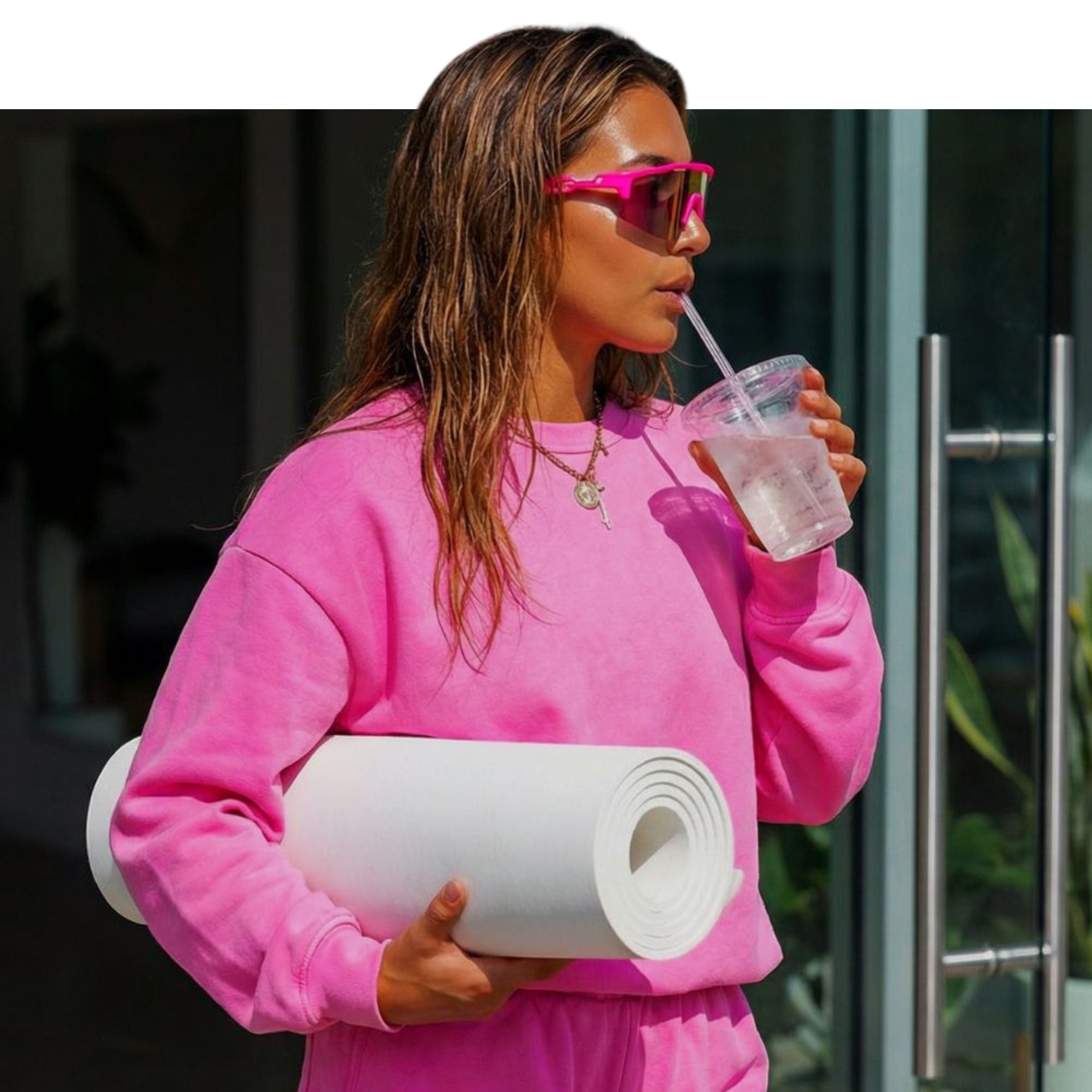 Person in pink outfit holding a yoga mat and drinking from a straw outside waring Solaro Shades sports sunglasses