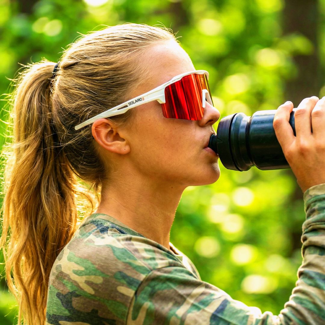 Person drinking from a water bottle with Solaro Shades biking sunglasses on, surrounded by greenery.