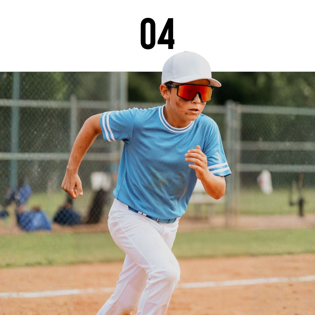 Child in a blue shirt and Solaro Shades kids sunglasses and white pants running on a baseball field with sunglasses.