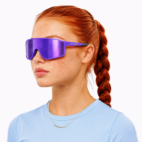 Person wearing a blue shirt and purple solaro sunglasses with a white background