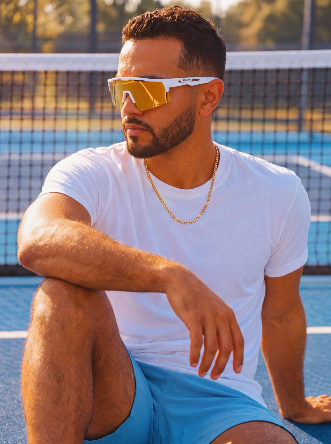 Man wearing white Solaro sunglasses with gold mirrored lenses on a blue court
